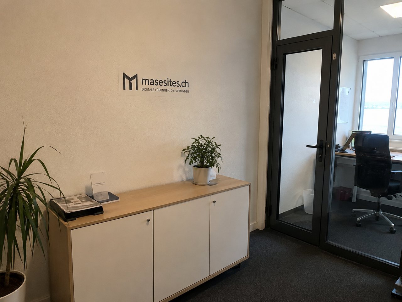 Empfang im Büro von masesites: das masesites.ch-Logo an der Wand über einem Sideboard, dahinter der Arbeitsraum mit Schreibtisch